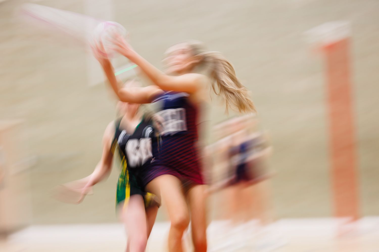 Blurred motion shot of netball players in action during an indoor game.