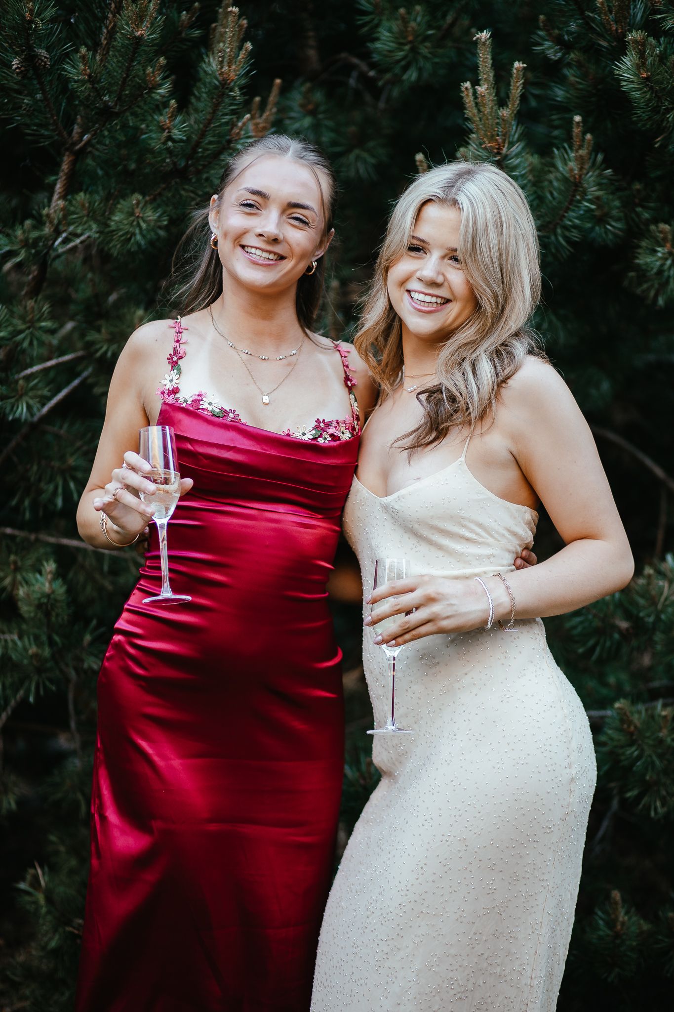 Friends in formal dresses sharing champagne and laughs outdoors.