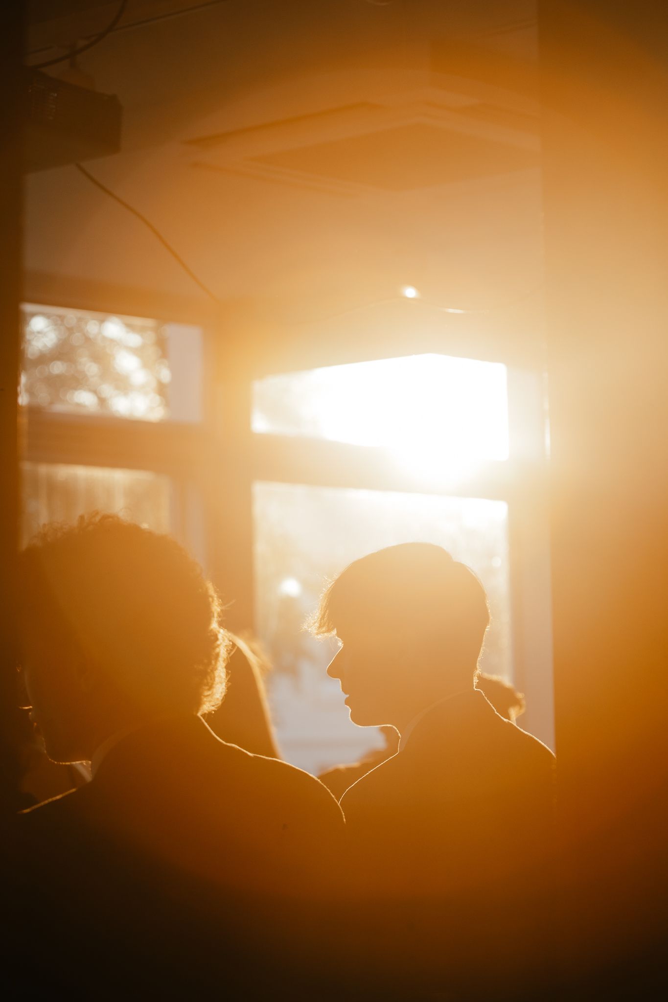 Silhouettes of guests highlighted by warm sunset light through windows at an evening event.