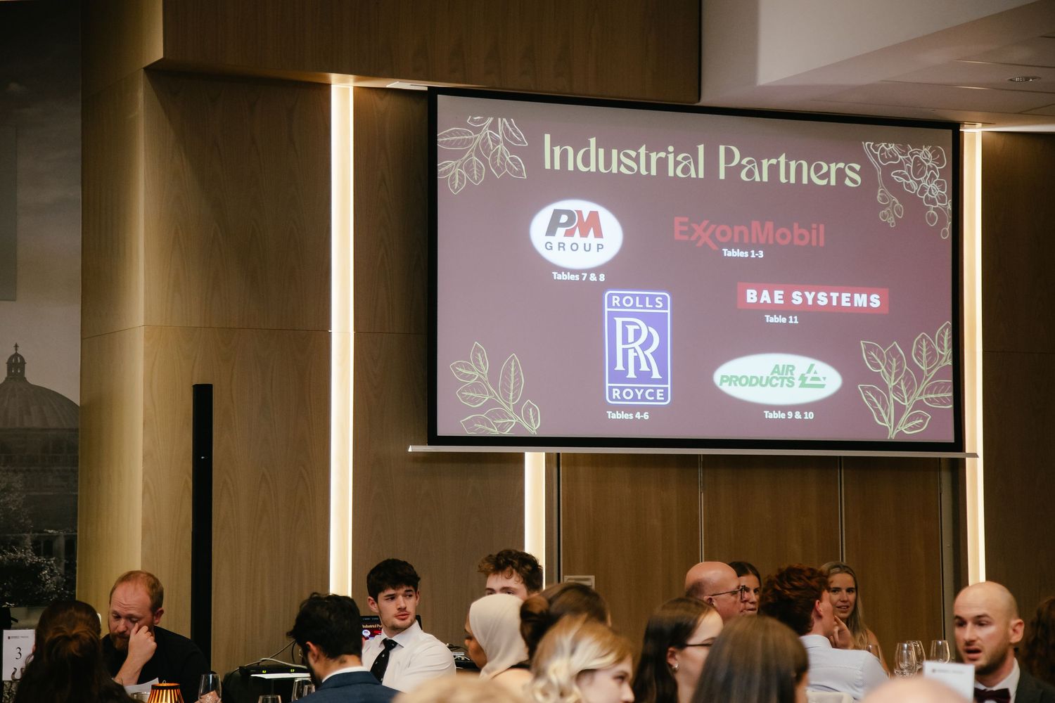 Corporate event with sponsor logos displayed on screens in a dimly lit conference venue.