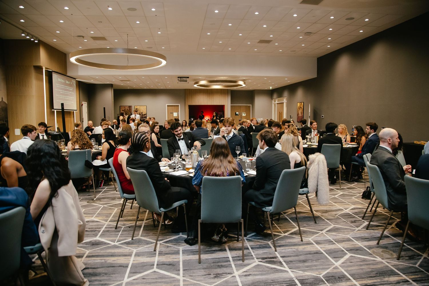 Large banquet hall filled with guests seated at round tables for formal dinner event.