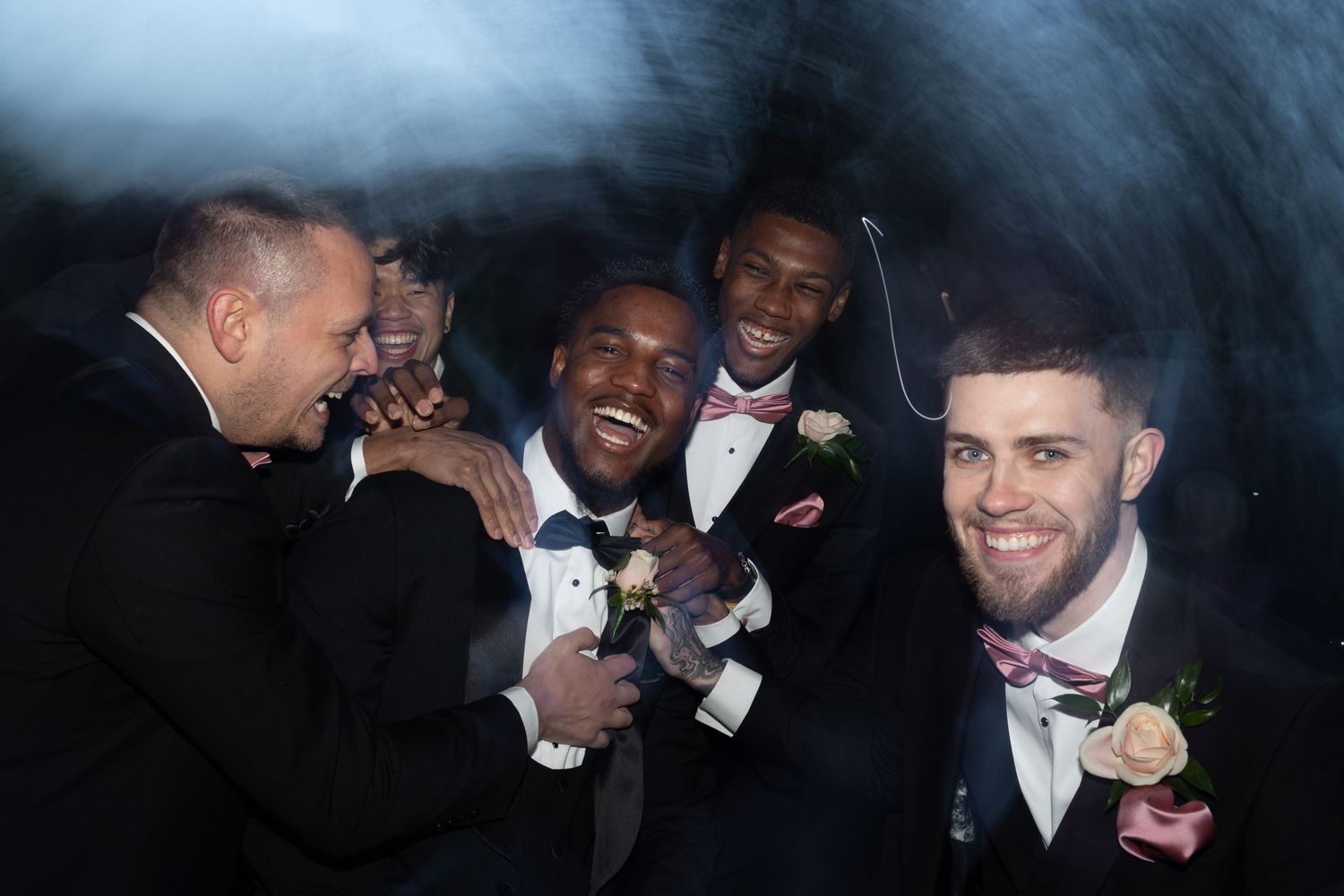 A group shares joyful laughter while dressed in formal black tuxedos at an elegant event.