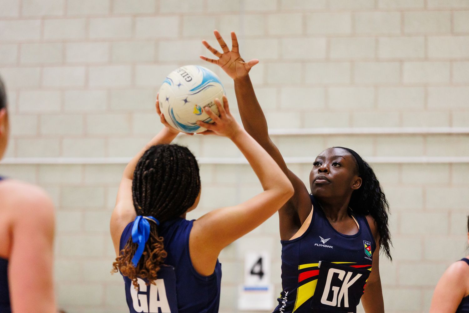 Players reaching up to catch a netball during an intense indoor game.