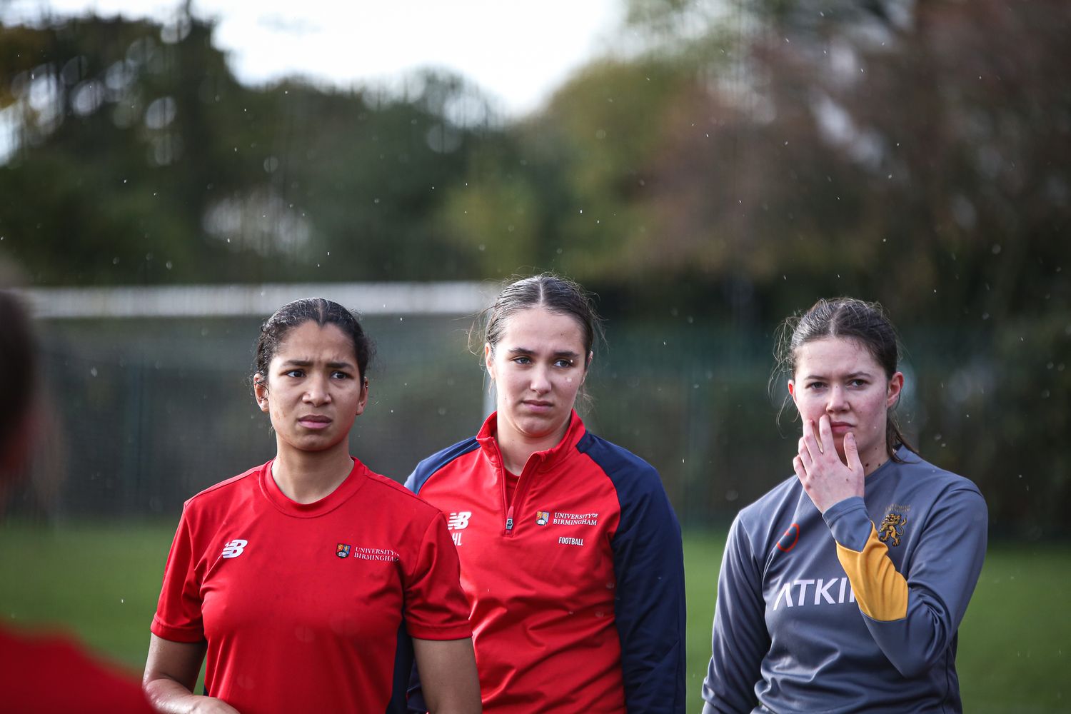 Athletes in red and grey uniforms gathered on a sports field during practice.
