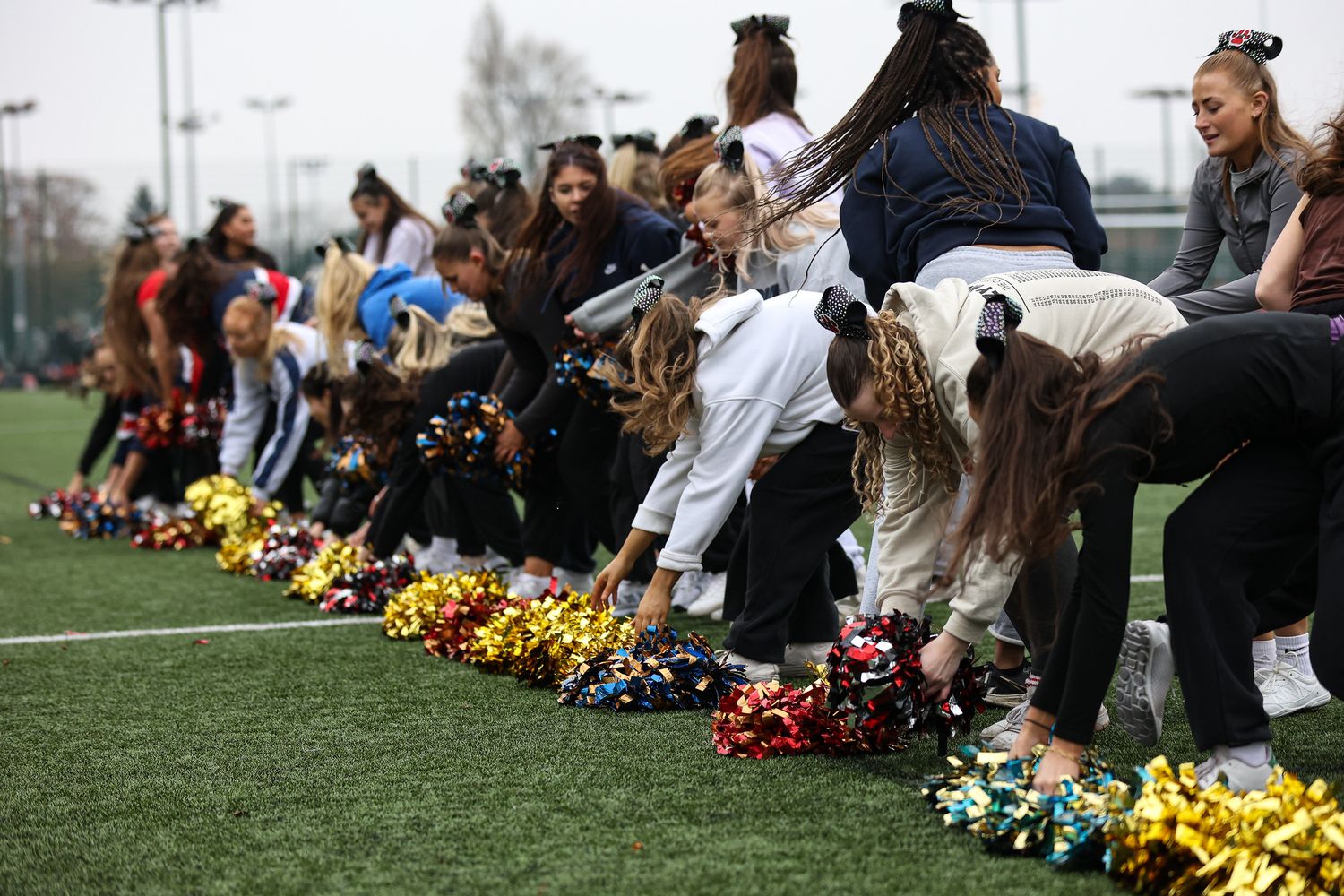 Students sit in a long line on grass during a memorial service with colorful flowers placed in front of them.