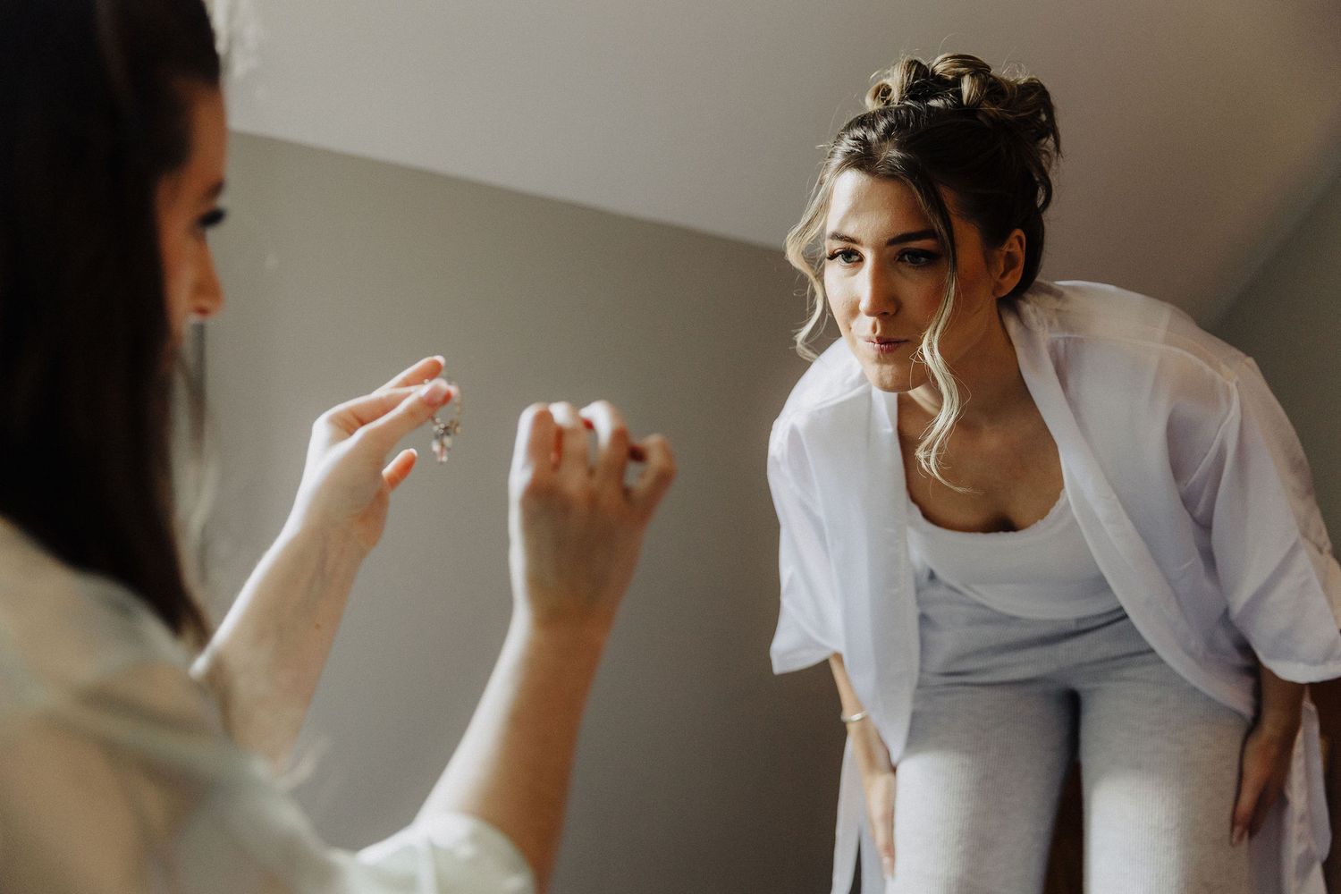 Bride in white robe getting ready, examining wedding ring with hair styled elegantly before her ceremony.