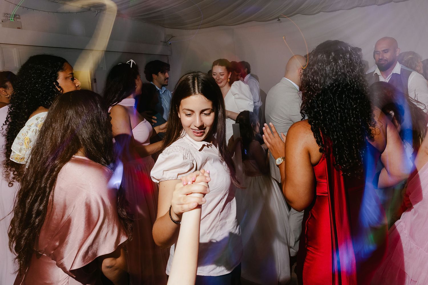 Guests dancing joyfully at a wedding reception party in a white tent venue.