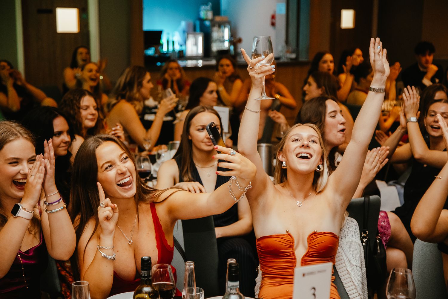 Enthusiastic crowd cheering with raised hands during a wedding reception celebration.