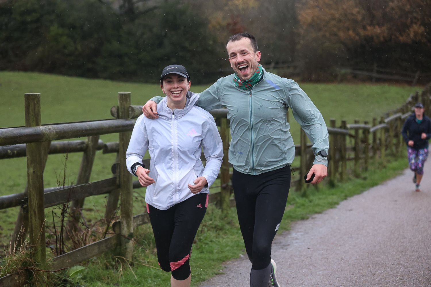 Two runners sharing a moment while jogging along a countryside path with wooden fencing.