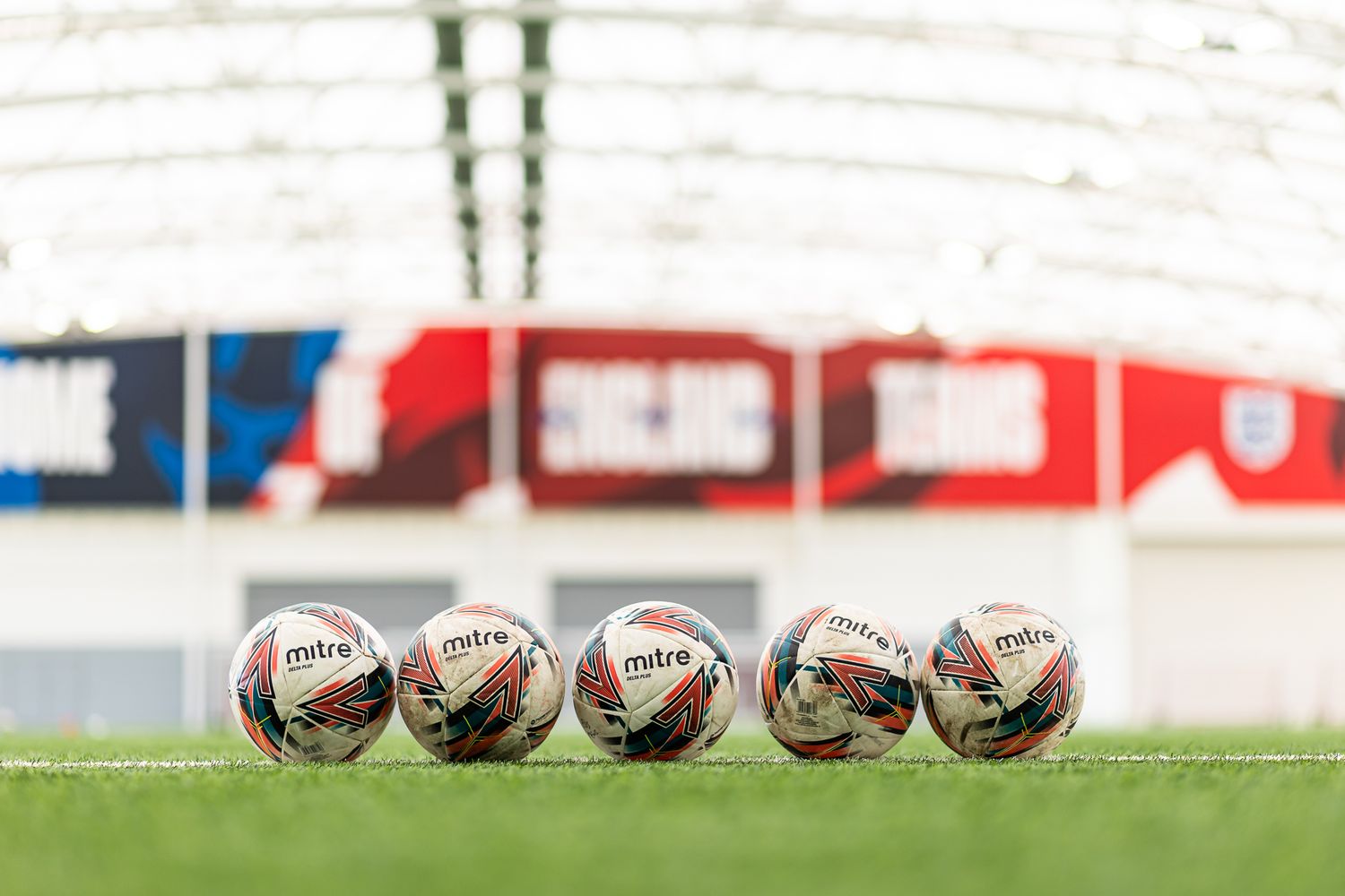 Row of rugby balls lined up on artificial turf field inside indoor sports facility.