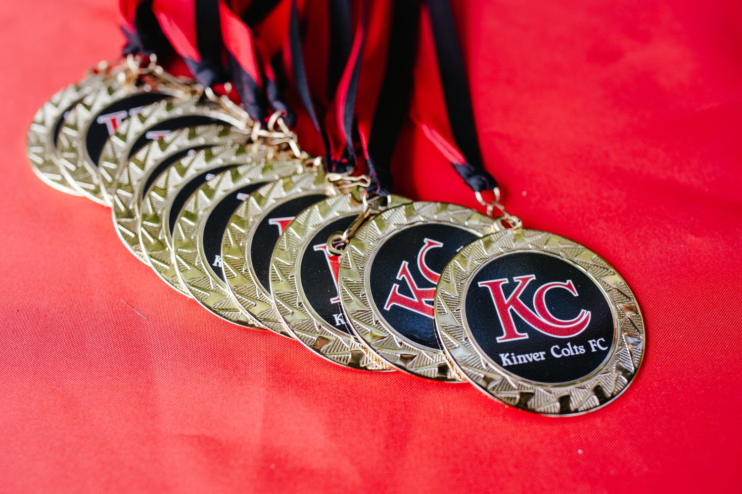 Gold medals with KC logo displayed on red background showing award recognition.