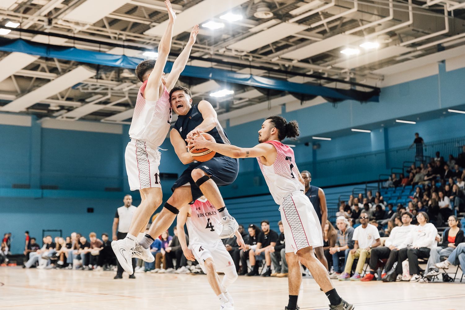 Wide angle shot of basketball players in action with crowd visible in background.