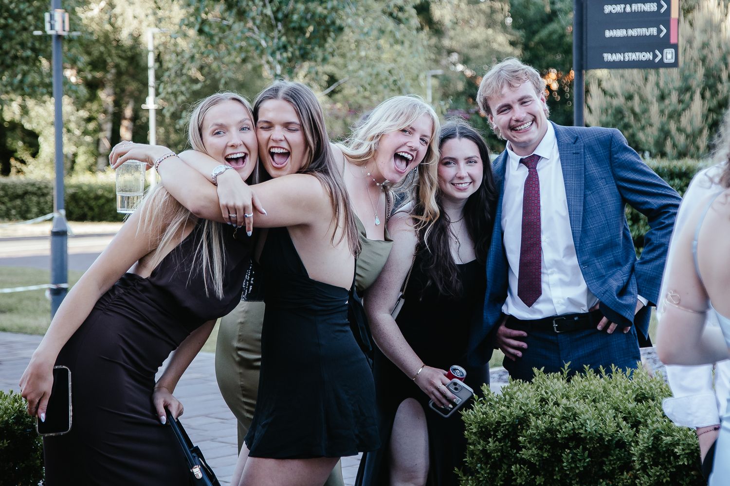 A joyful group of friends laughing together outdoors in formal attire.