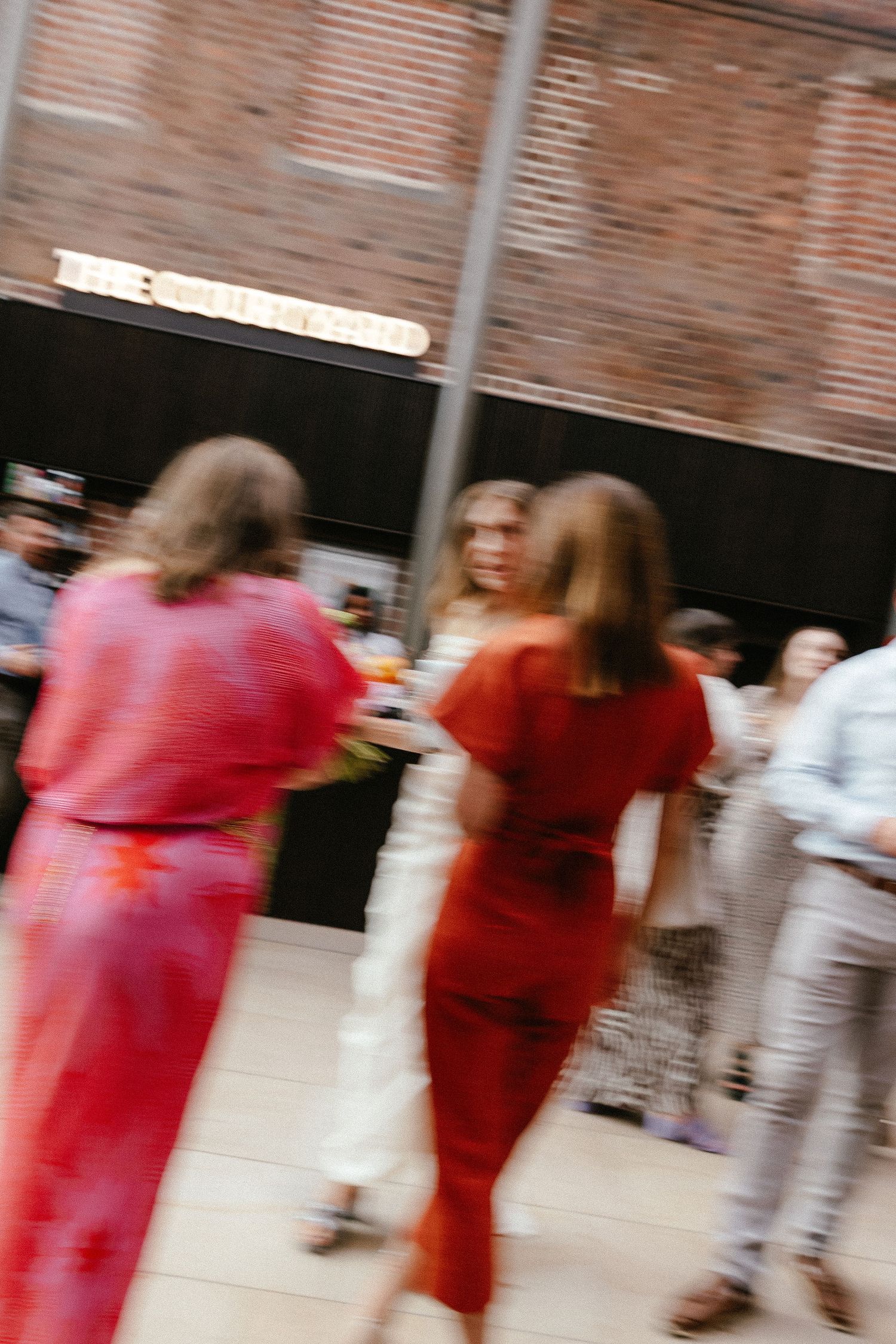 Blurred motion shot of guests in red outfits socializing at an indoor event venue with brick walls.