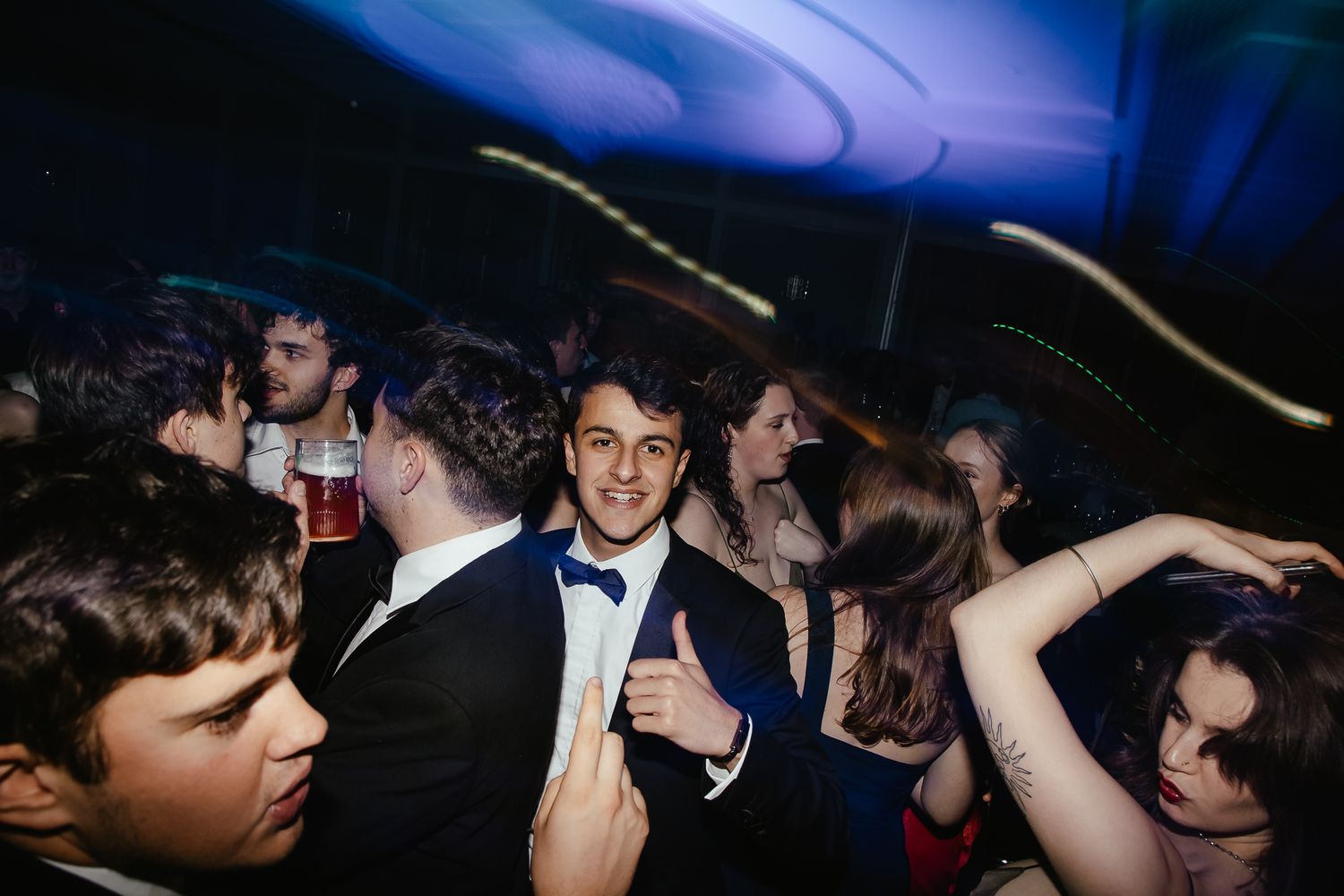 Crowd of people dancing and celebrating under blue mood lighting at a nighttime event.