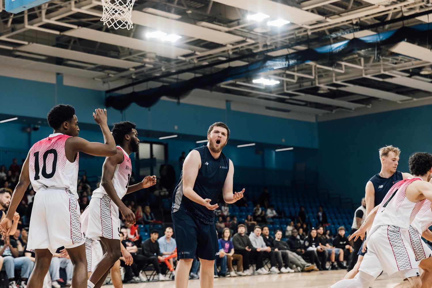 Wide shot of an indoor basketball court with players lined up during a game.