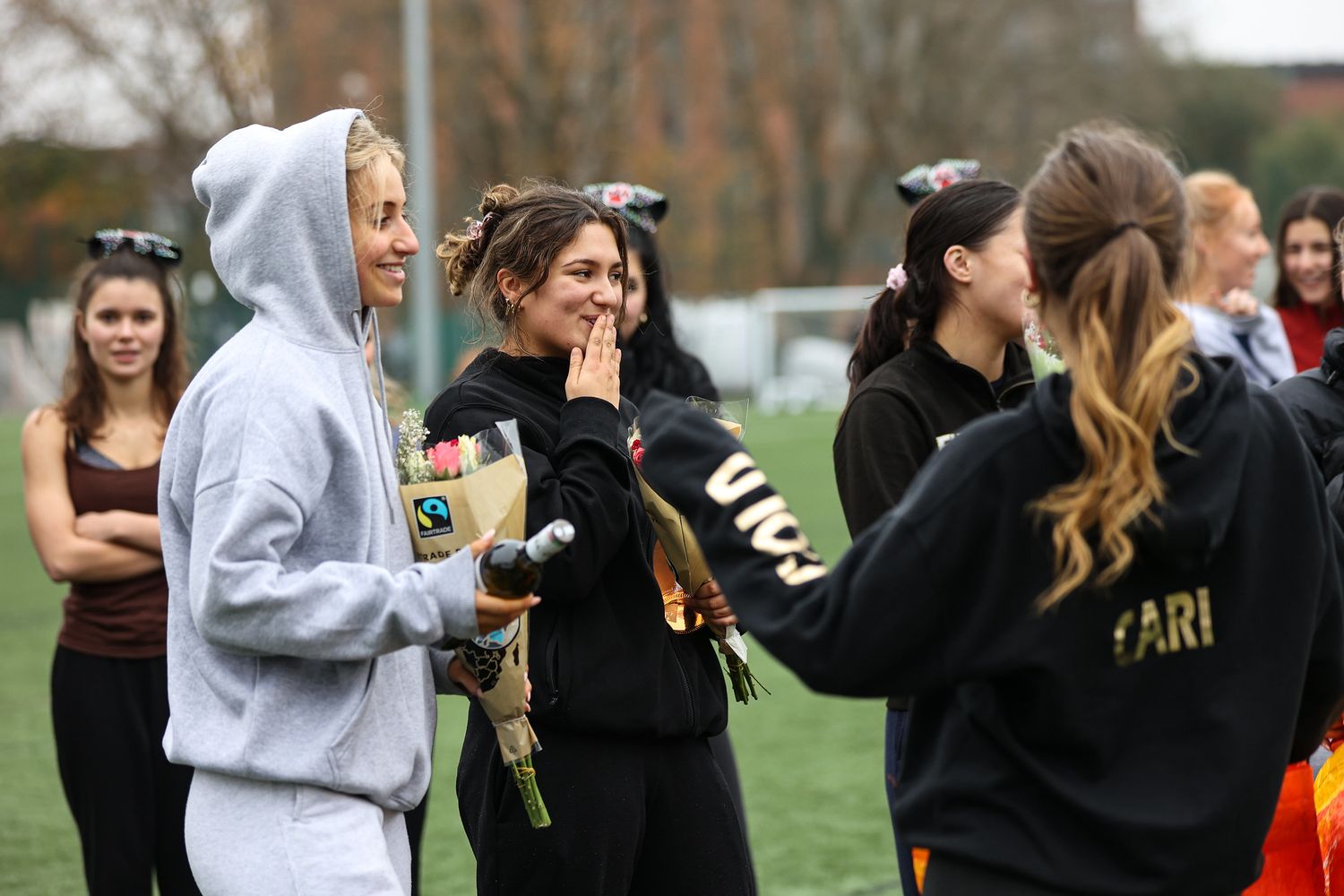 College students gather on a sports field for an outdoor social event with drinks and casual attire.