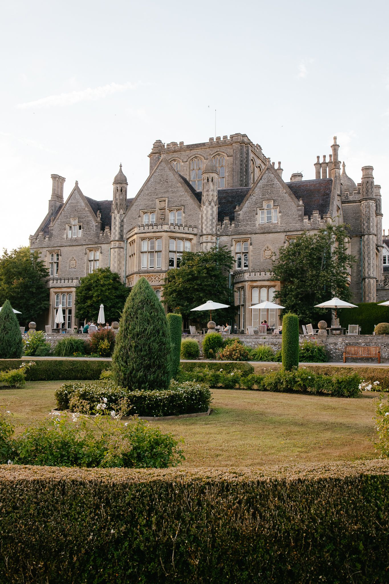 Wedding photography at the De Vere Tortworth Court mansion with manicured gardens, hedges and patio umbrellas on sprawling grounds.