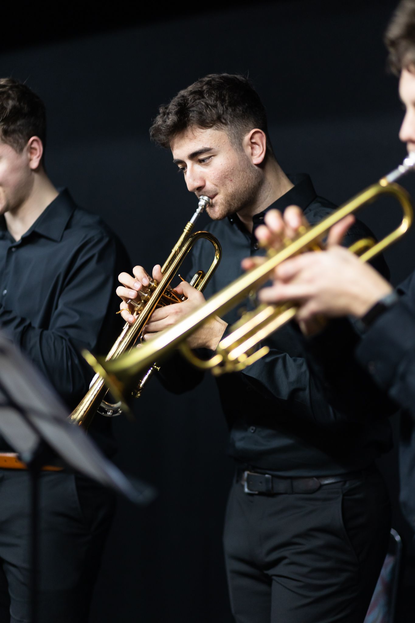 Musicians in formal black attire perform with trumpets during a concert.