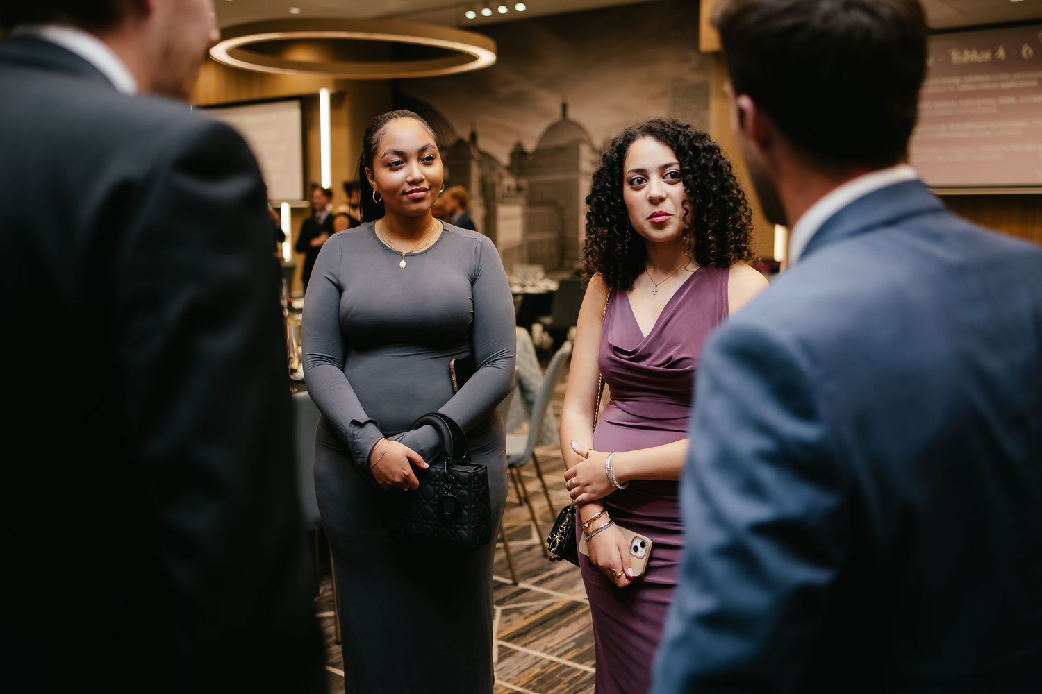 Business professionals having a conversation in a hotel lobby with modern circular lighting fixtures overhead.