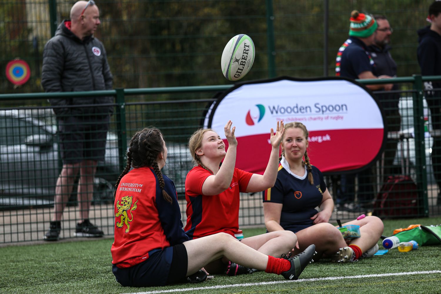 Rugby equipment and players resting on sidelines during a match break.