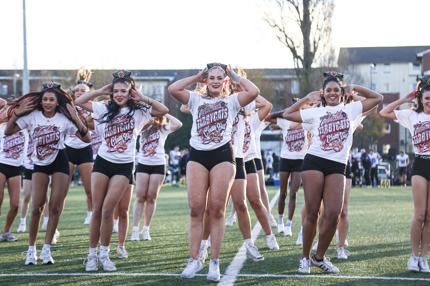 Cheerleaders in black uniforms perform synchronized dance moves during an outdoor routine performance.