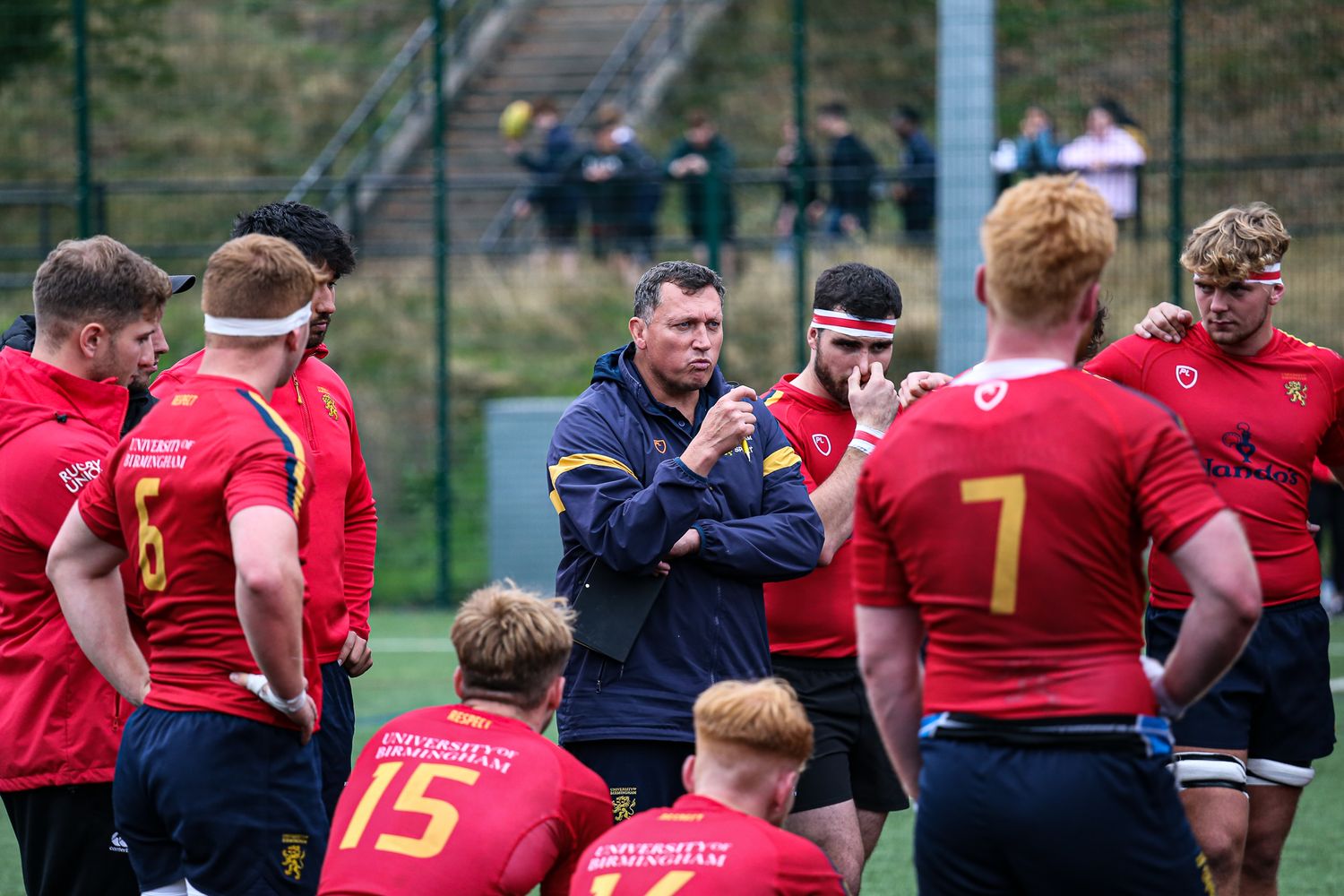 Rugby players in red and navy uniforms competing intensely during a match on a grass field.