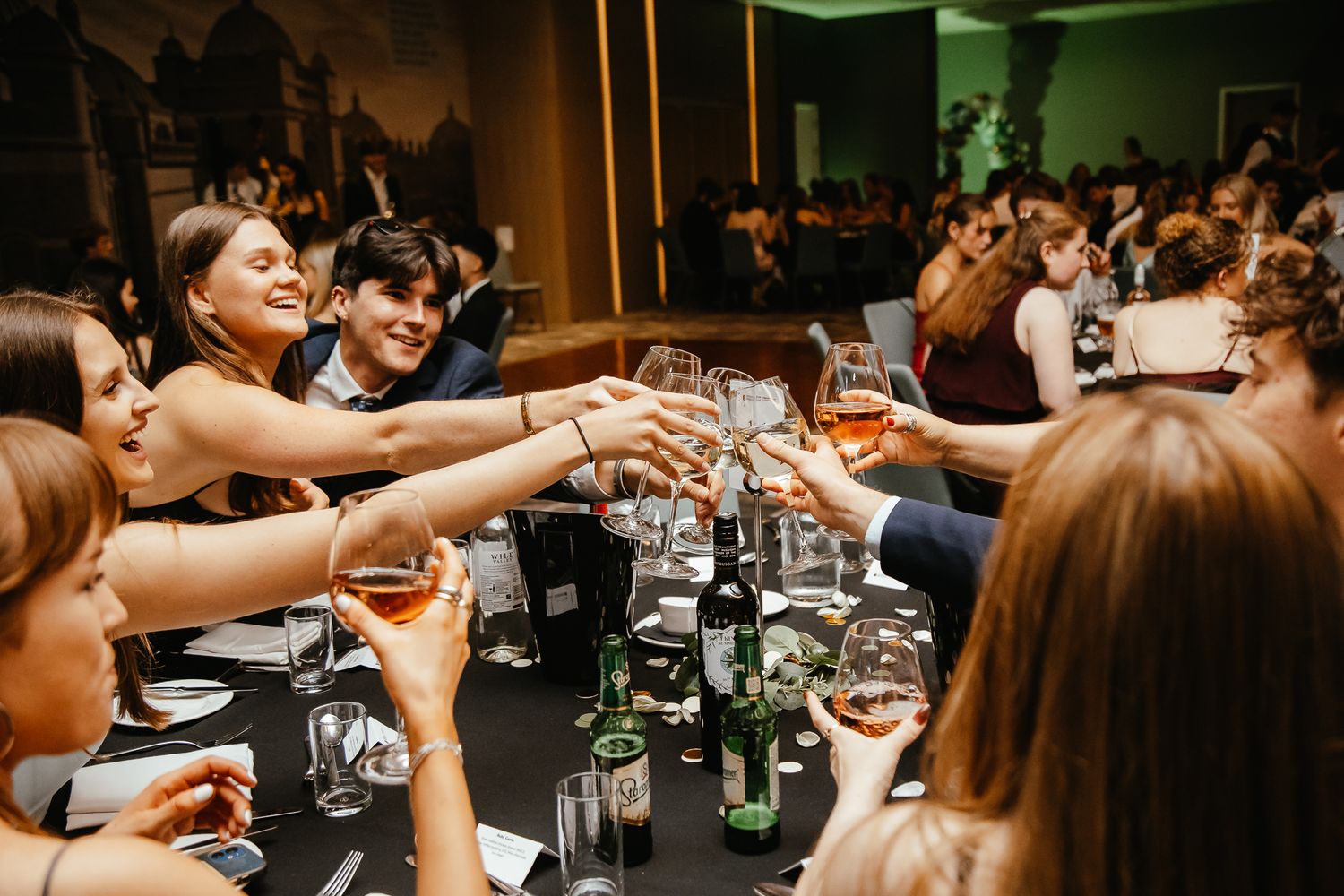 Wedding guests raising glasses and cheering across long dining tables.