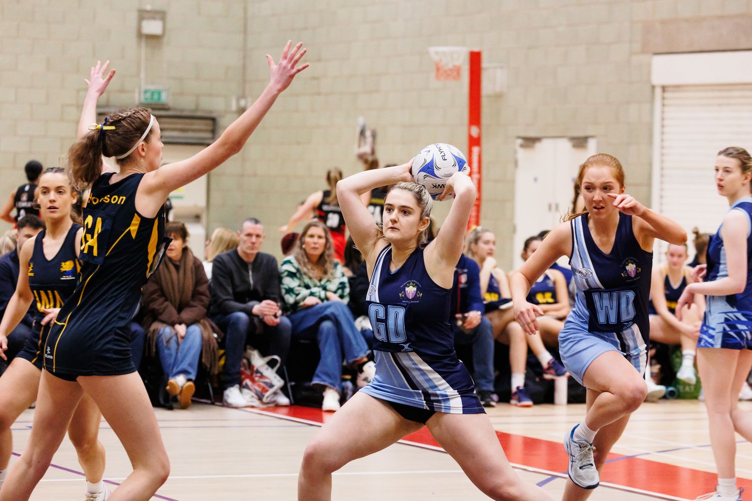 Action sequence of netball players jumping and moving during an indoor game.