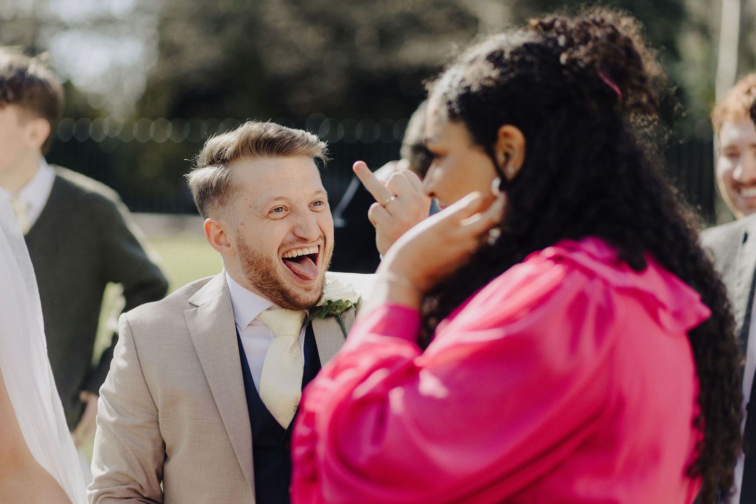 Laughing groom in grey suit sharing a joyful moment with a guest at his wedding.