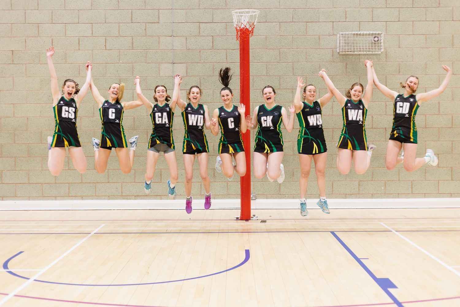 Team of netball players in green uniforms standing in formation on an indoor court during practice.