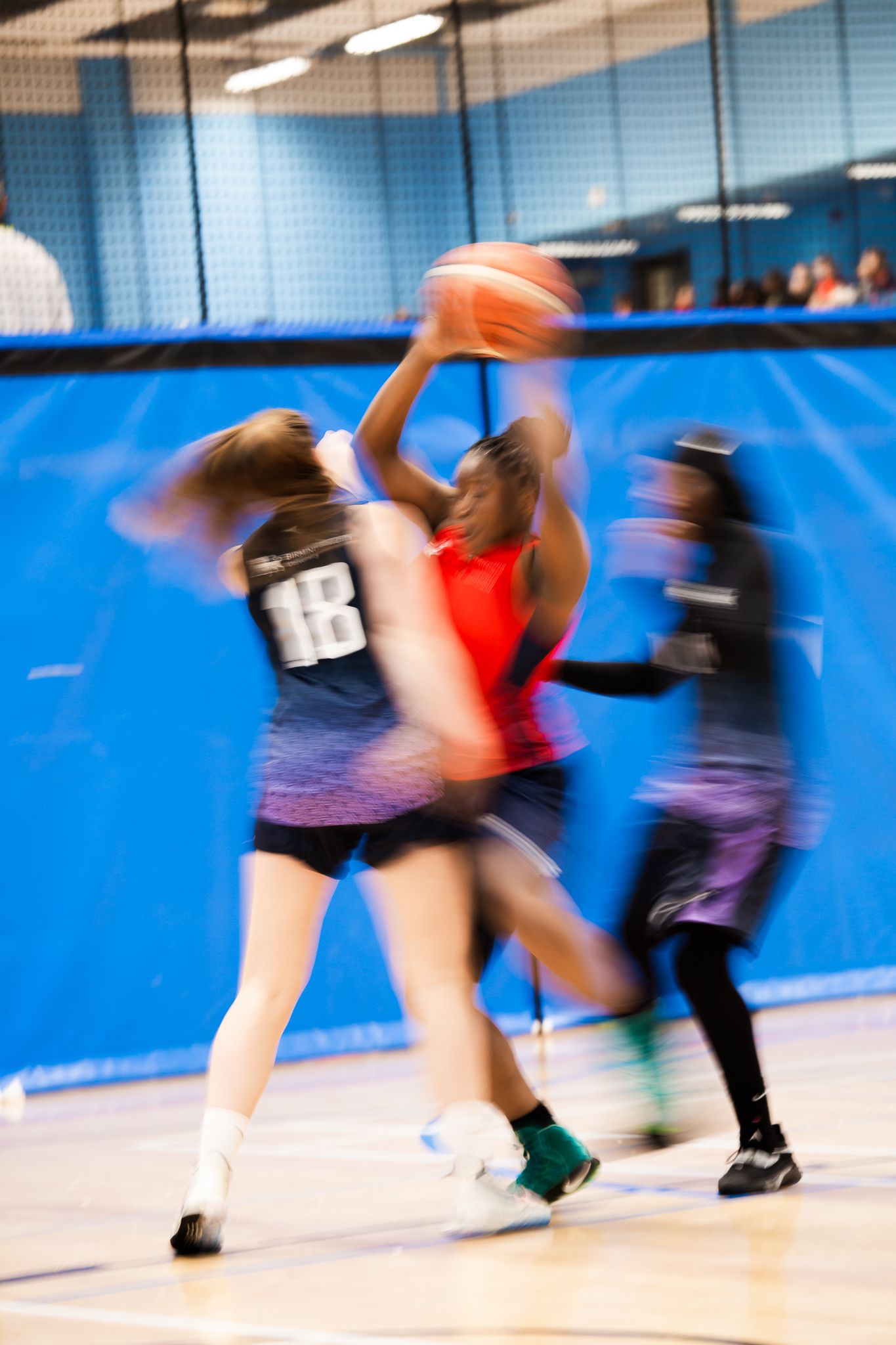Motion-blurred players competing in an indoor sports match with blue walls.