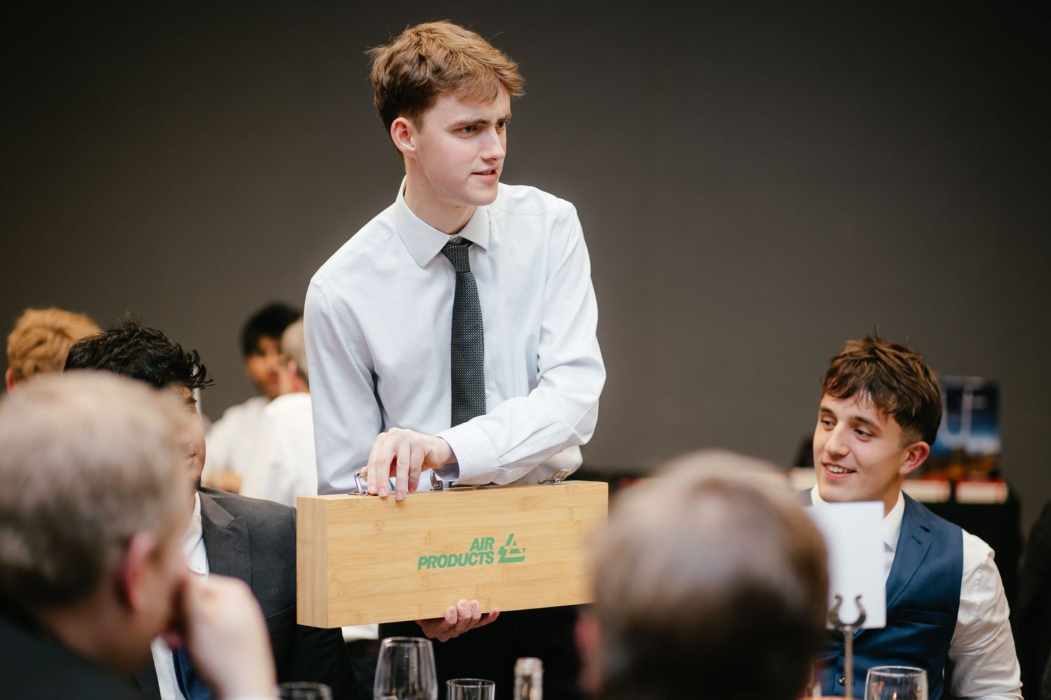 Server carrying a wooden box through a formal dining event.