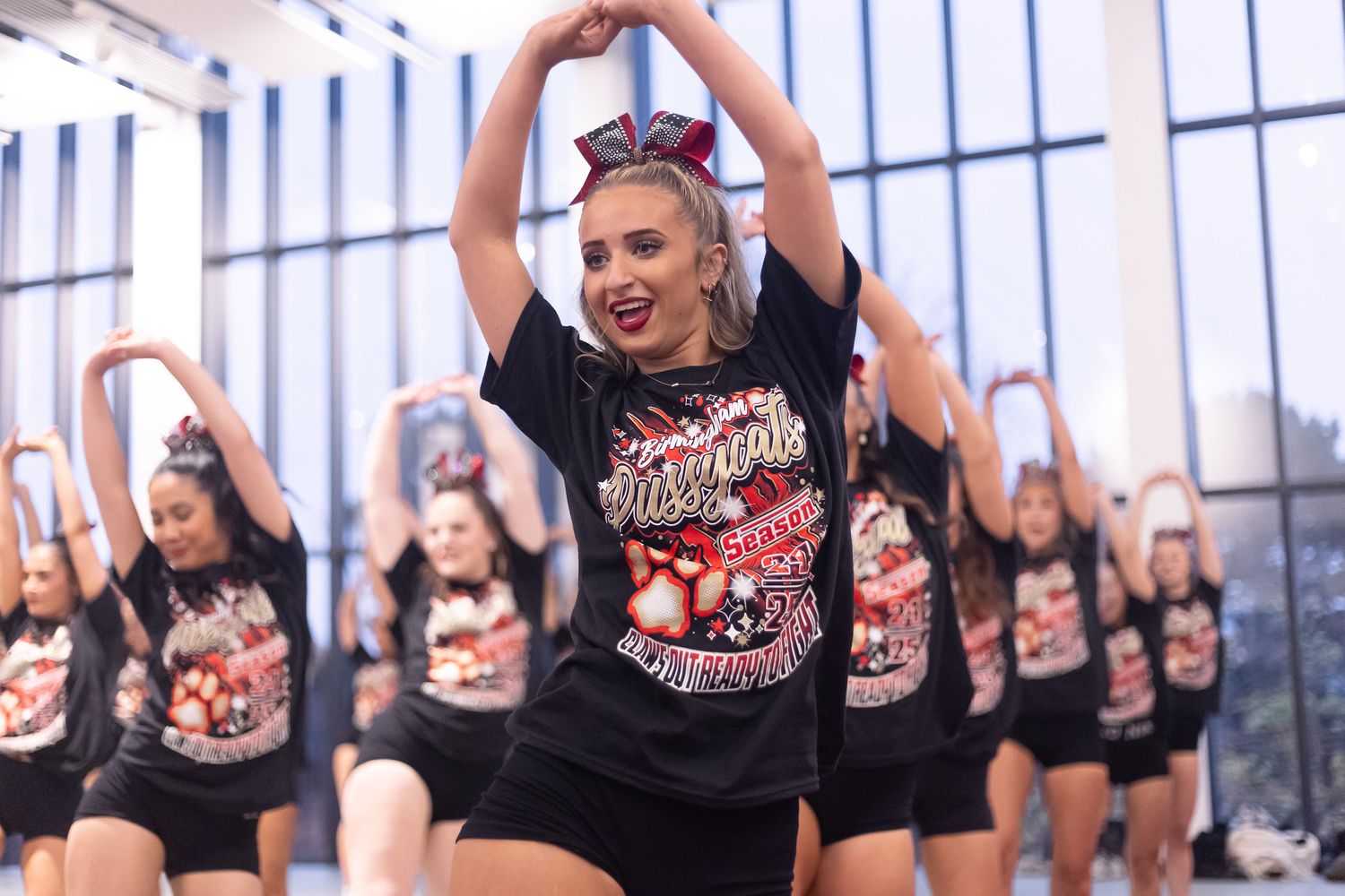Cheerleaders in black uniforms perform a synchronized dance routine during a high-energy performance.