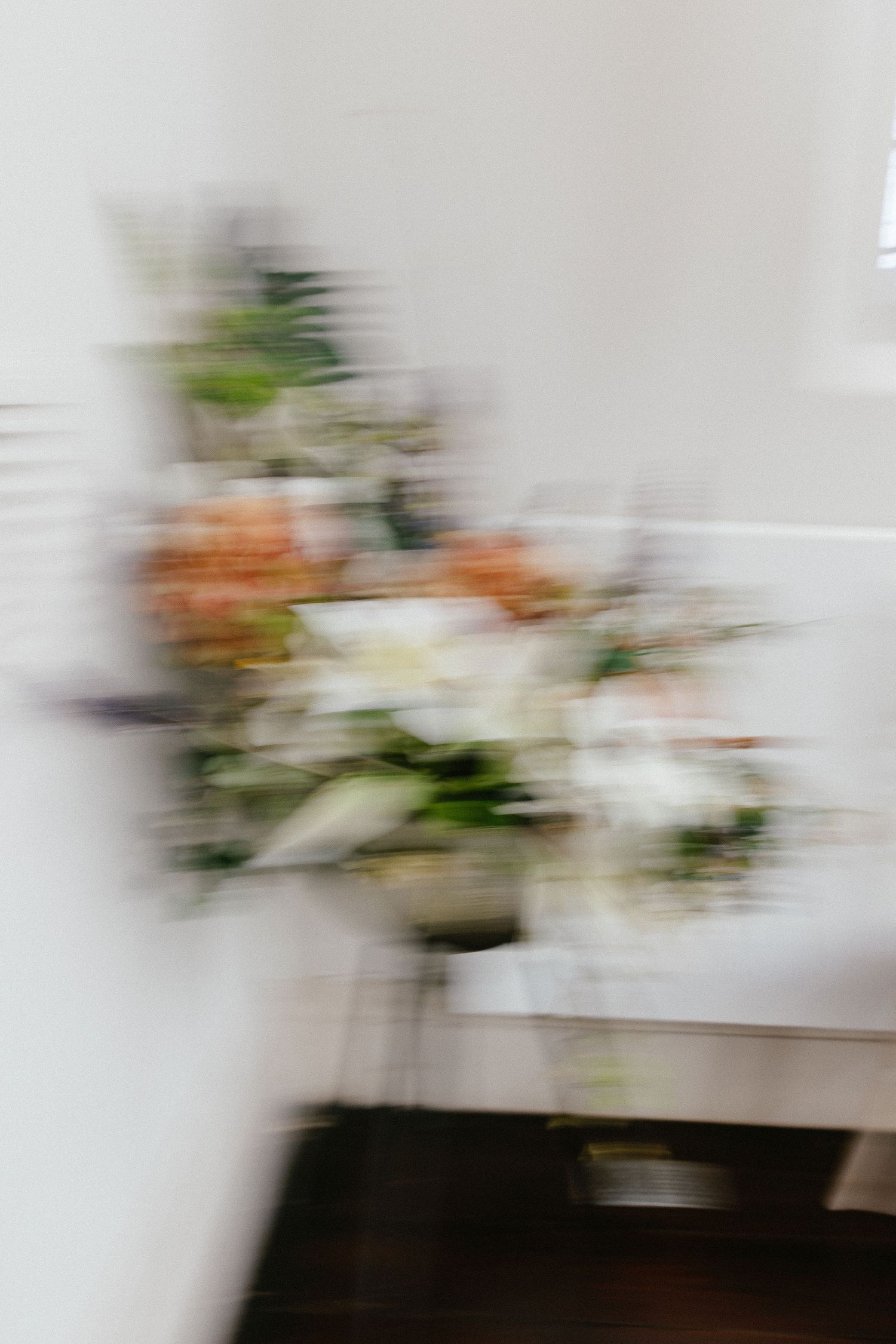 Blurred floral arrangement with white and peach blooms displayed on white shelving in a bright interior setting.