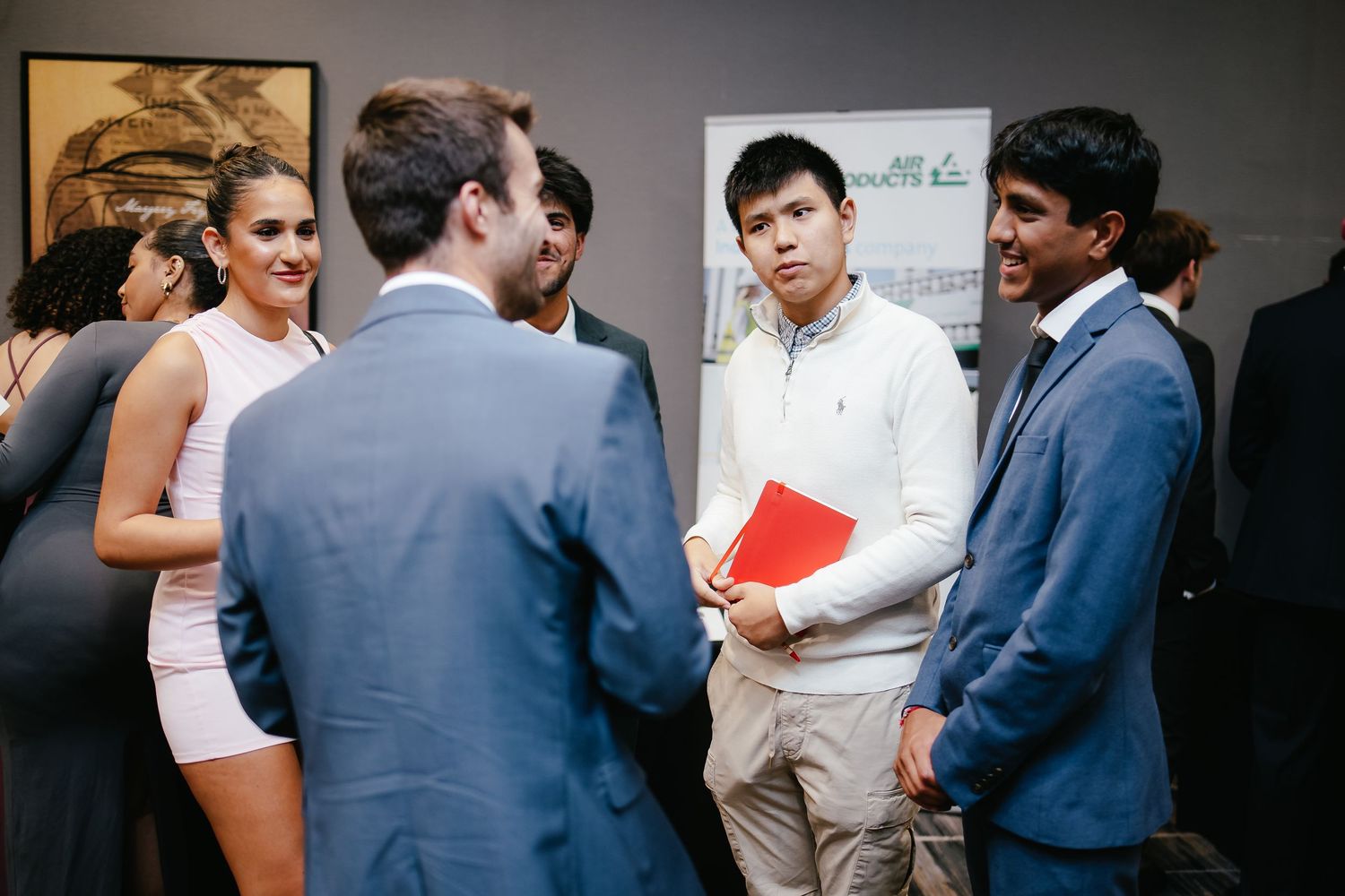 A group of young professionals in business attire having an informal conversation in an office setting.