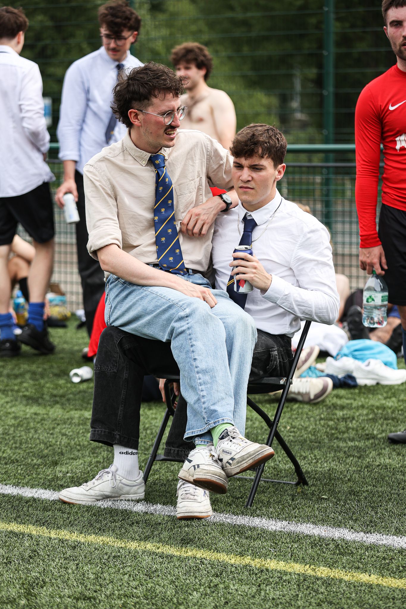 Players resting on chairs along the sidelines of a soccer field during a break.