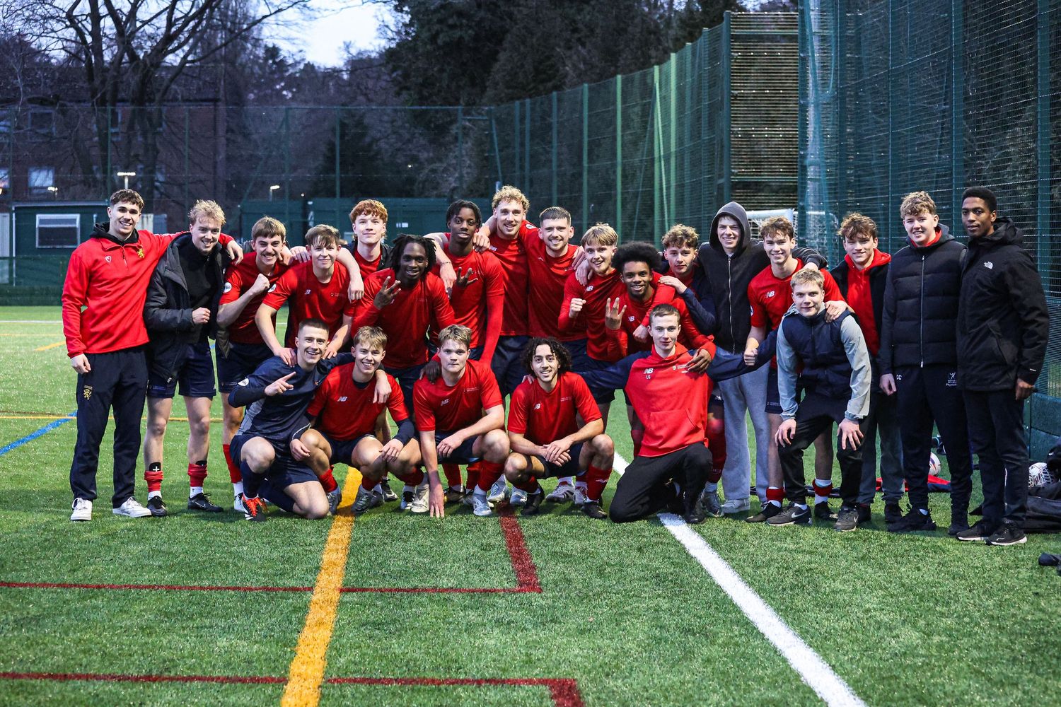 Team photo of soccer players and staff posing together on artificial turf field.