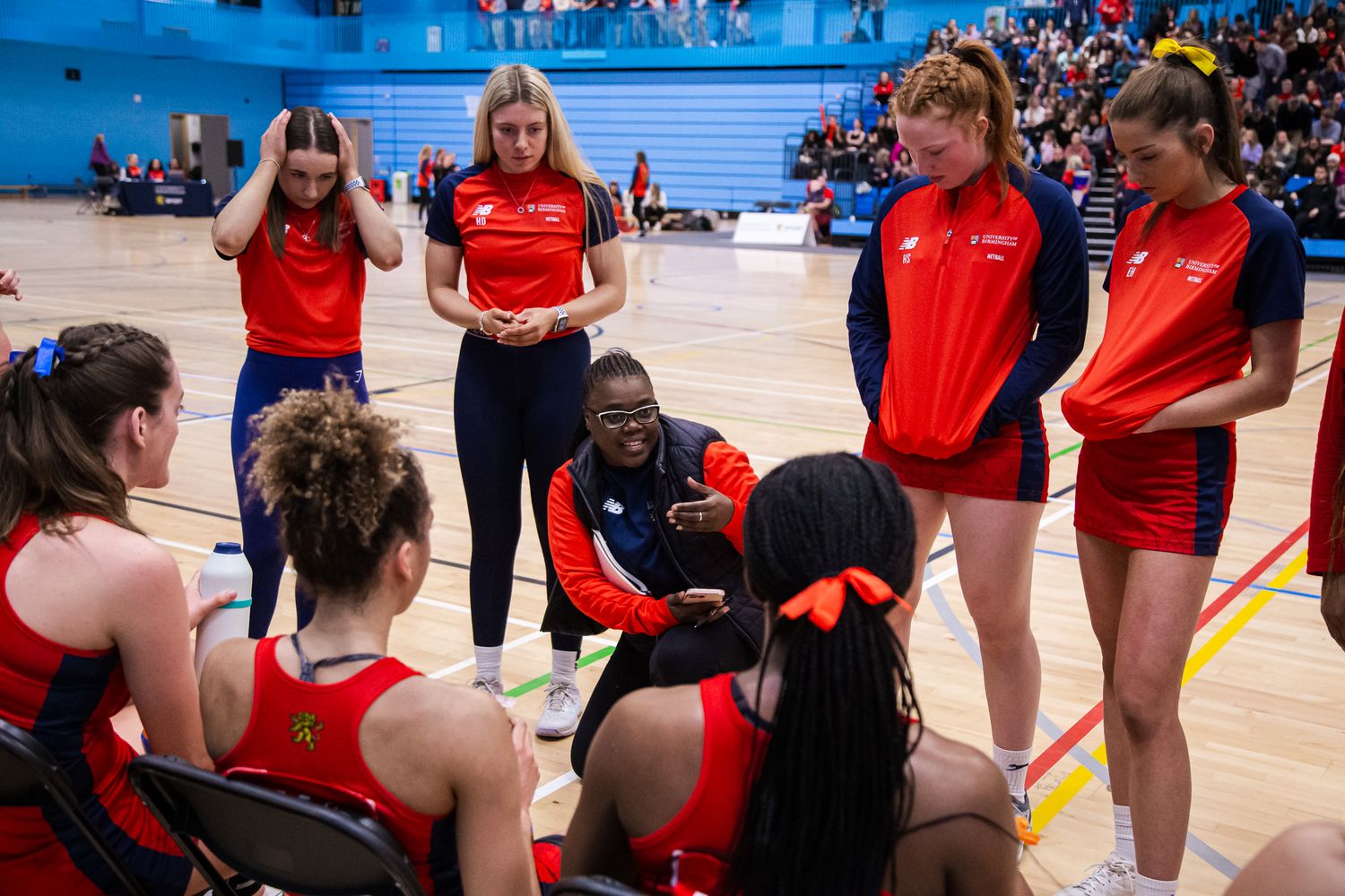 Sports team members interacting on sidelines during indoor game.