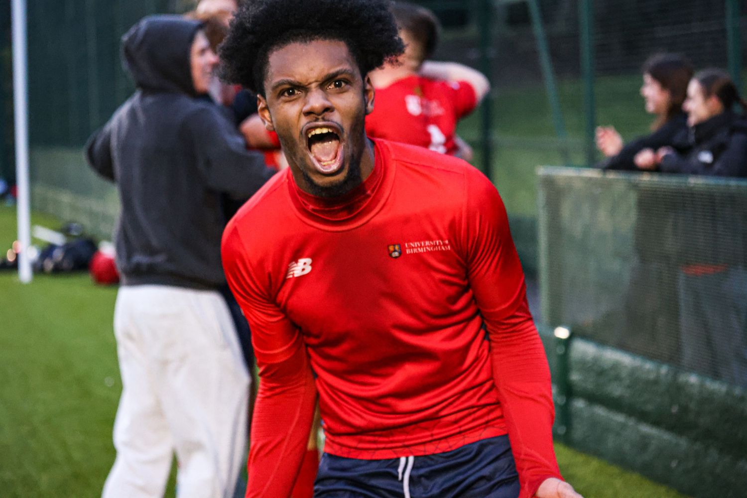 Soccer player in red New Balance jersey expressing joy and excitement on the field.