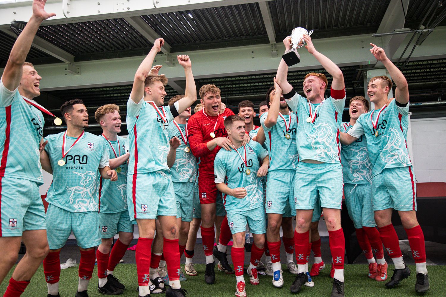 Soccer team celebrating with raised arms while wearing turquoise jerseys during practice.