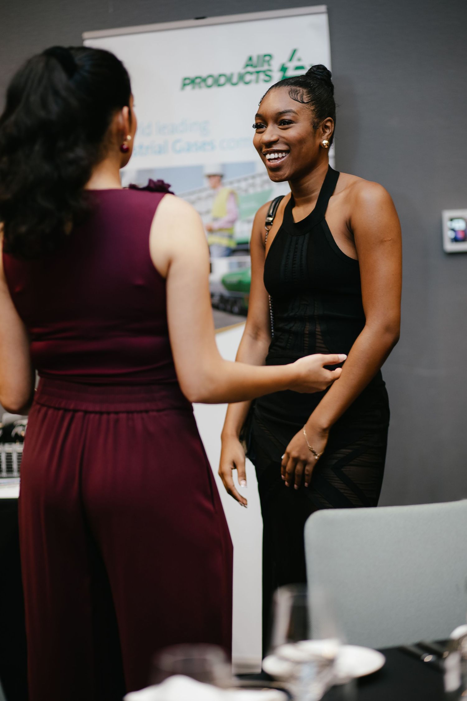 Two people in burgundy dresses share a joyful moment at an office event.