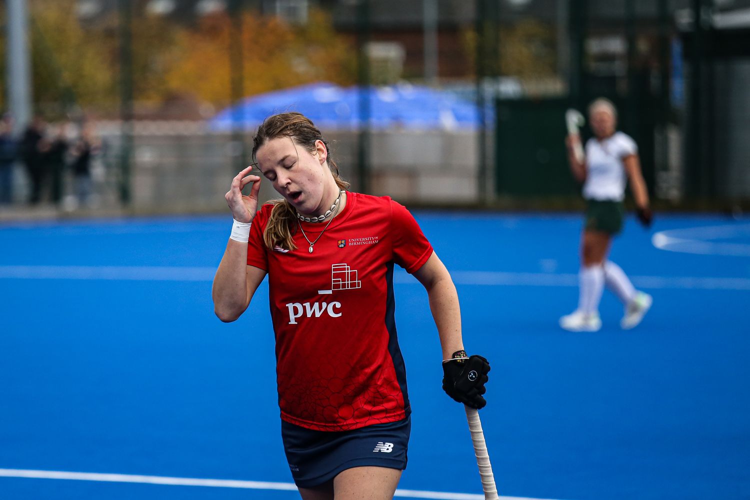 Athletes in red uniforms playing field hockey on a blue turf field.