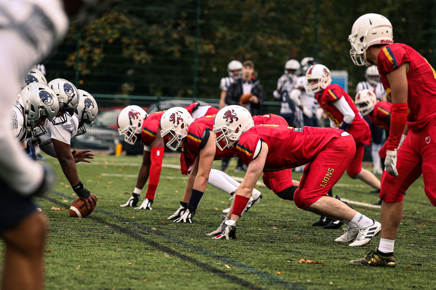 Football players in red and white uniforms line up at scrimmage during a game on grass field.