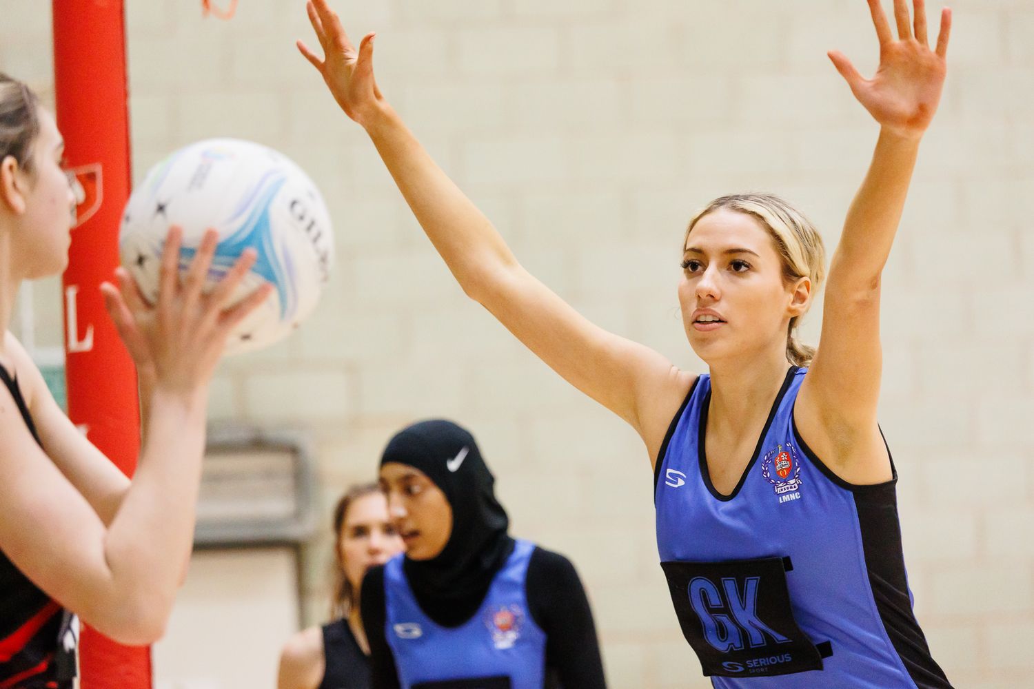 Athletes in blue and red uniforms competing for possession during a netball match.