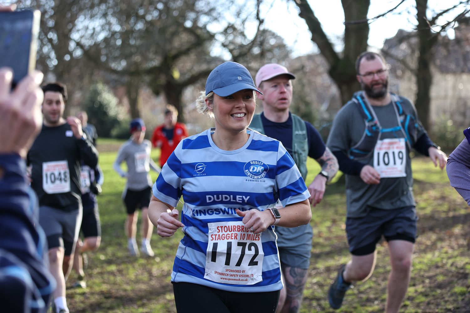 Runners competing in a cross country race through a wooded course wearing race bibs.