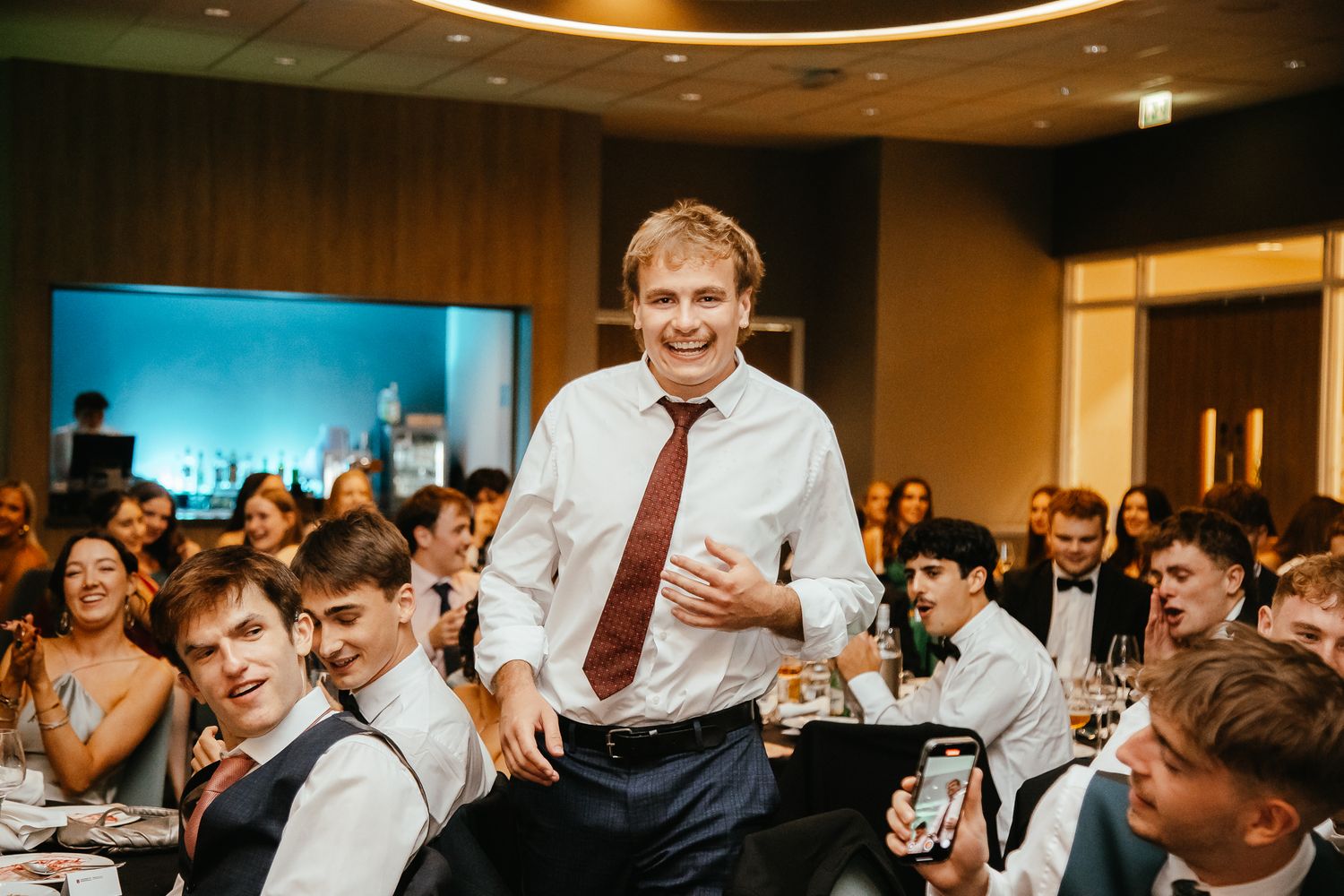 Large group celebrating at an elegant indoor venue with circular lighting fixtures overhead.