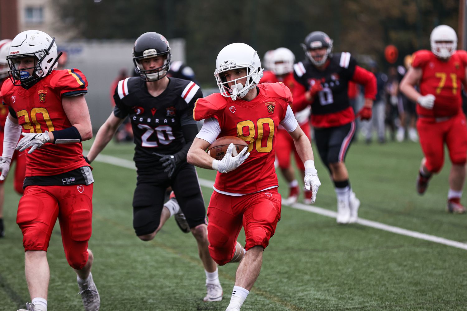 Football players in red and black uniforms running drills during a practice session.