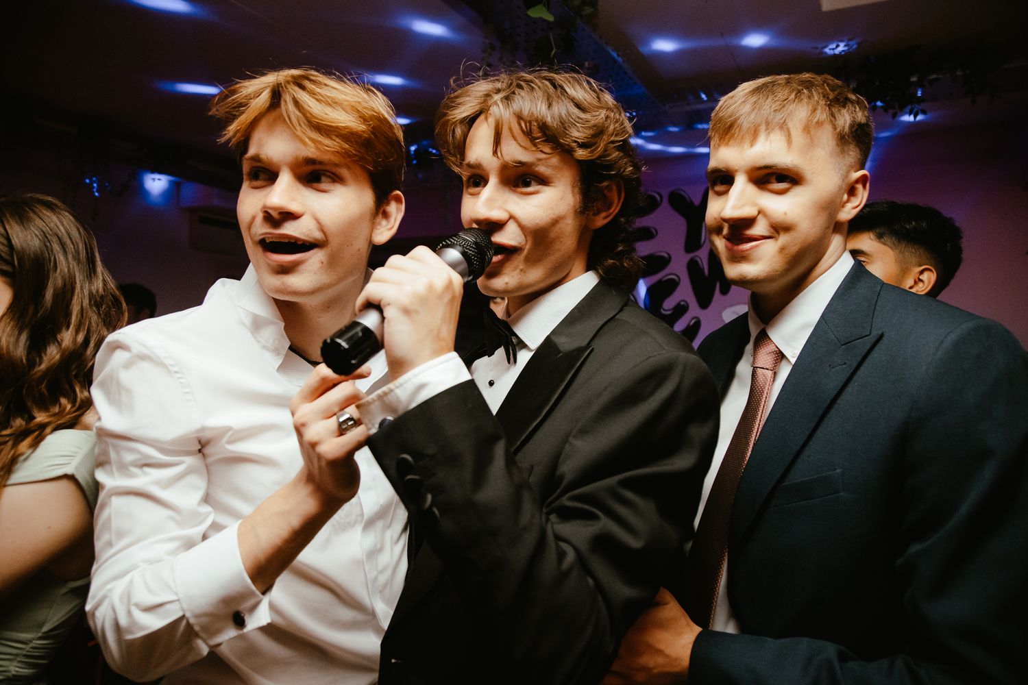 Wedding guests in formal attire dancing and celebrating under blue lighting.