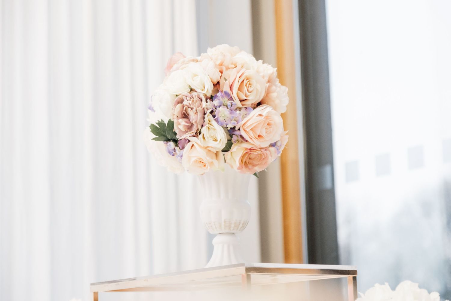 Soft pink and peach roses arranged in white vase against bright window.